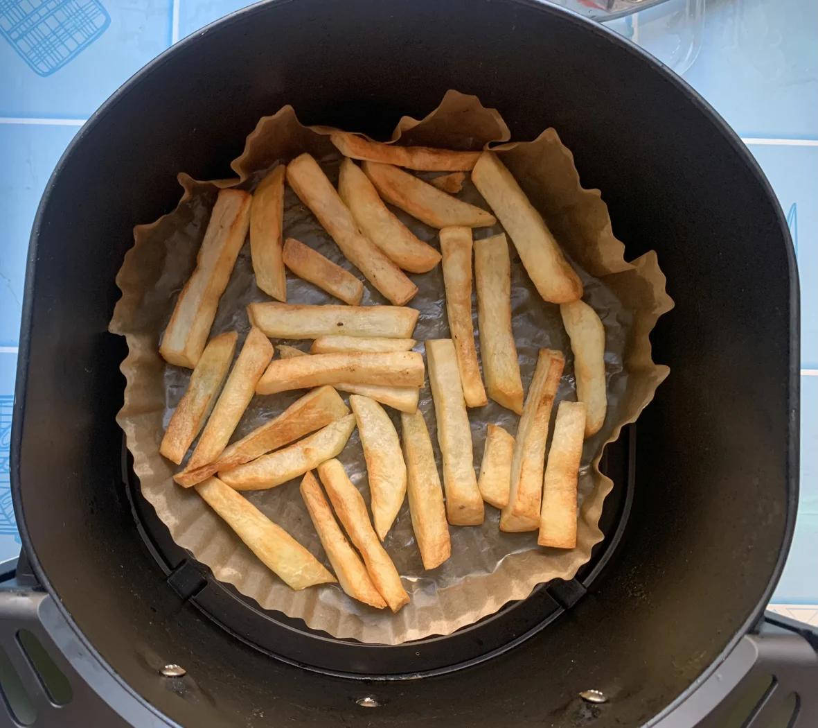 一口不锈钢锅中正在进行薯条预炸,油温适中,薯条呈半透明状漂浮于油面,旁边放置温度计显示150摄氏度,台面上有沥油网架和已炸好的浅黄色薯条 薯条双炸过程示意图