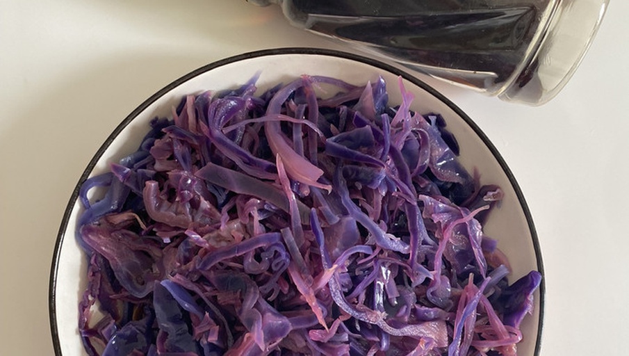 一个约5岁的小女孩坐在餐桌前,手中拿着半个紫红色的紫甘蓝馒头正开心地咬下一口,嘴角沾着些许紫色碎屑,背景为厨房环境,阳光透过窗户洒入,营造出温暖健康的饮食氛围 孩子开心地咬一口紫红色馒头的温馨场景