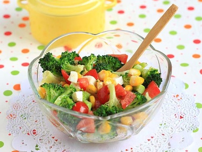 一位成年人正在用筷子夹起一碗色彩丰富的蔬菜沙拉，其中包含焯水后的西兰花、樱桃番茄、紫甘蓝和坚果碎