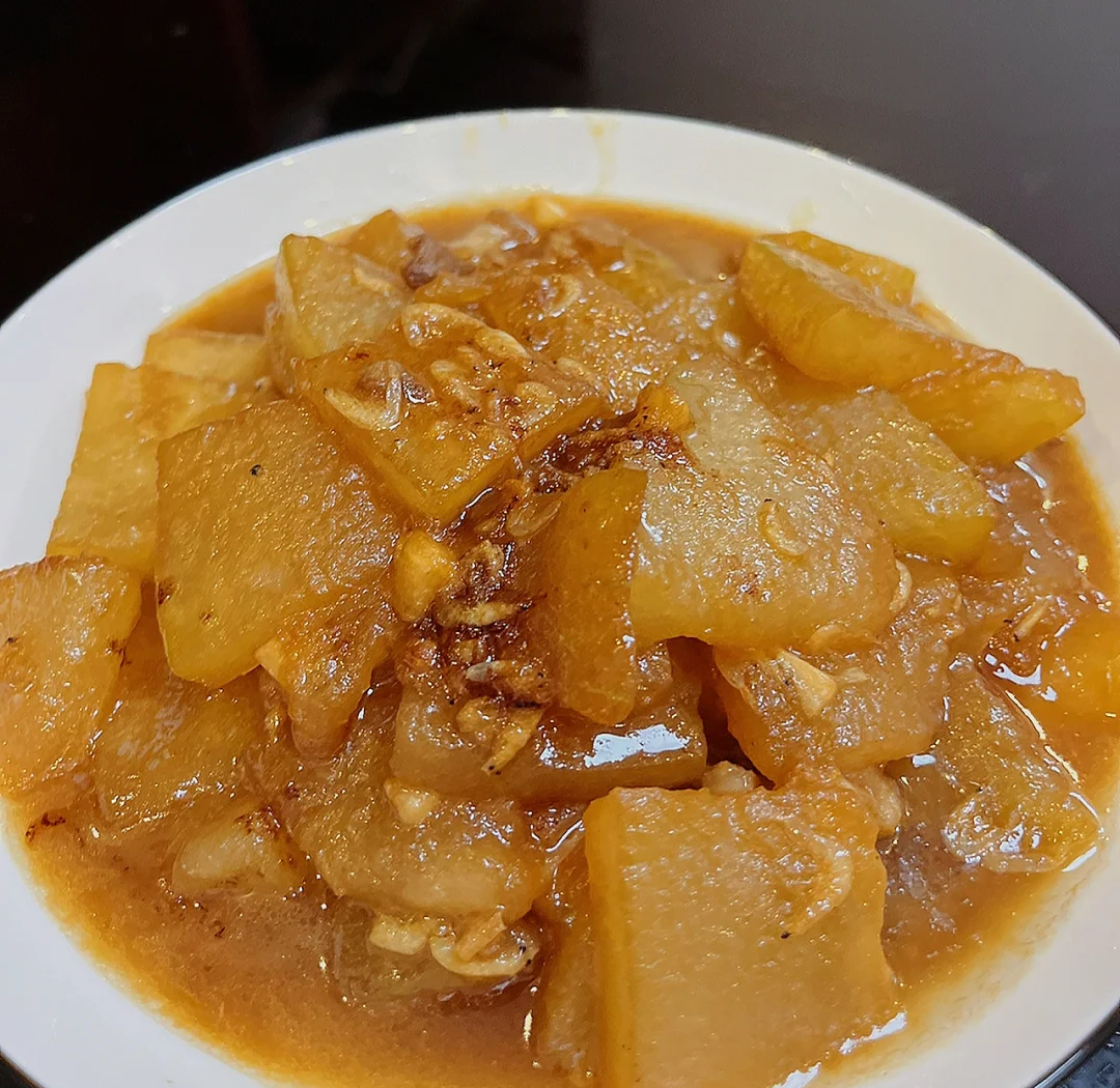 虾米冬瓜煲成品特写：深褐色砂锅中码放整齐的琥珀色冬瓜块，表面裹薄芡油亮，嵌着金黄虾米碎与翠绿葱花，汤汁浓稠挂勺