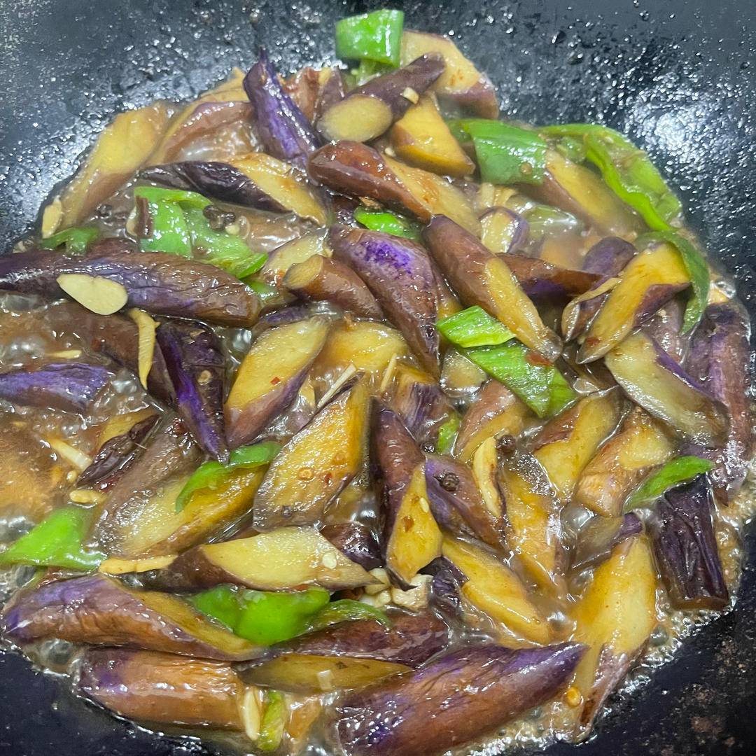 一位厨师正在家庭厨房中用不粘锅快速翻炒切片青茄,锅中青茄呈翠绿色,配有蒜末和少量红色辣椒,灶台旁摆放新鲜青茄原料和柠檬片,体现健康烹饪理念 家庭厨房烹饪场景