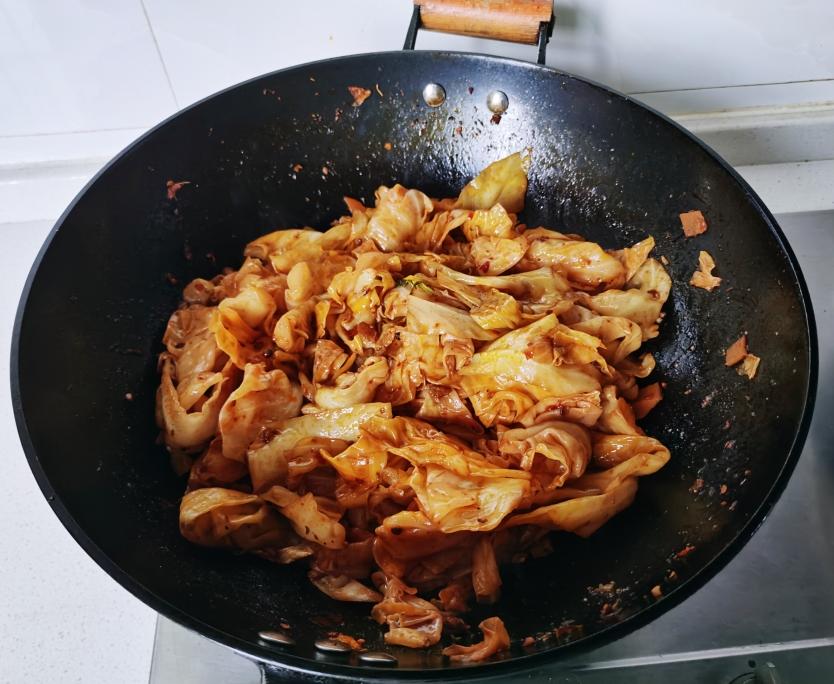 一位家庭主妇在厨房灶台前翻炒锅中的扁包菜,锅中菜叶翻飞,伴有淡淡蒸汽,旁边放着切好的蒜片和调料瓶,整体氛围温馨居家 家庭厨房中正在烹饪扁包菜的场景