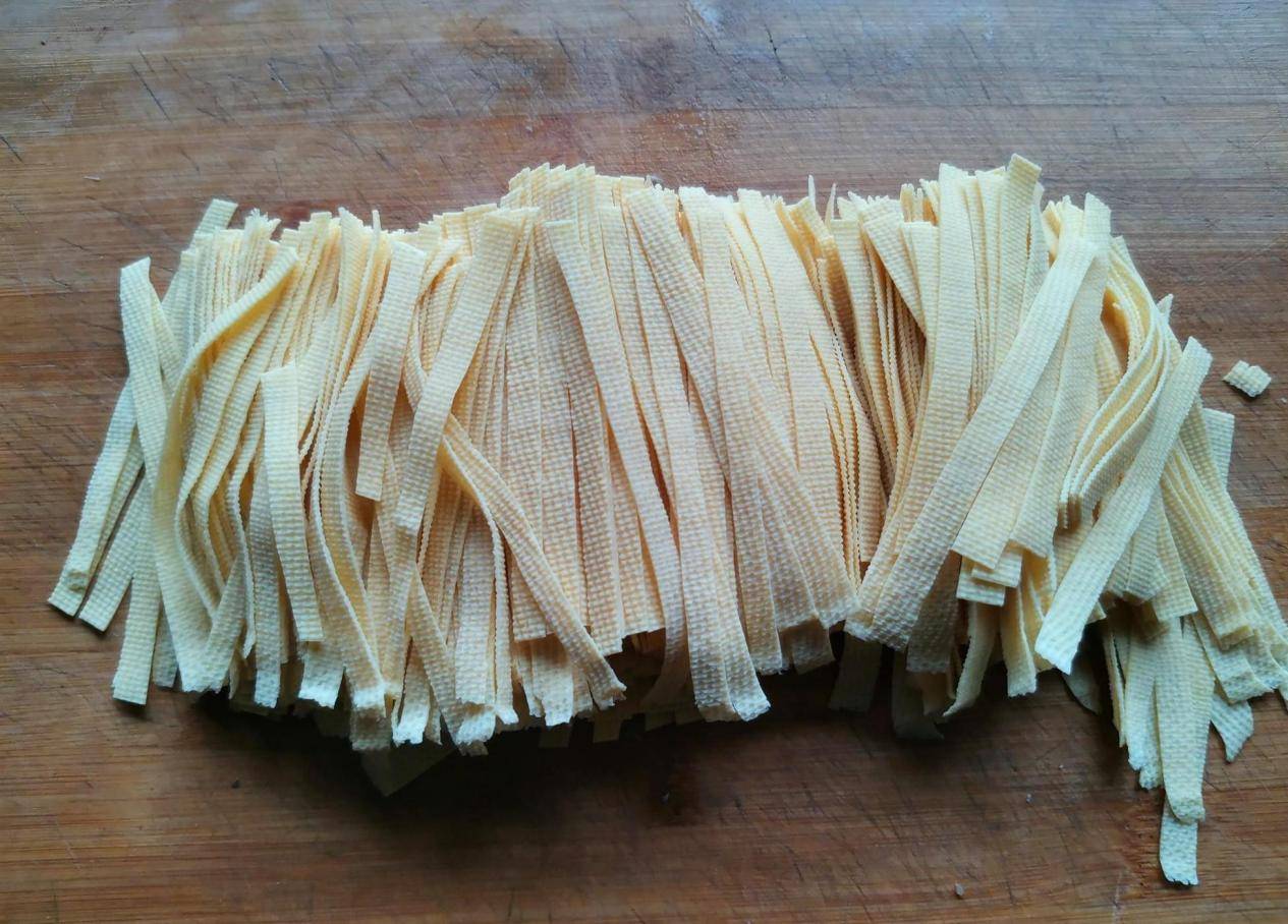 新鲜山芹与干腐竹摆放在木质砧板上，背景为厨房台面，自然光线明亮