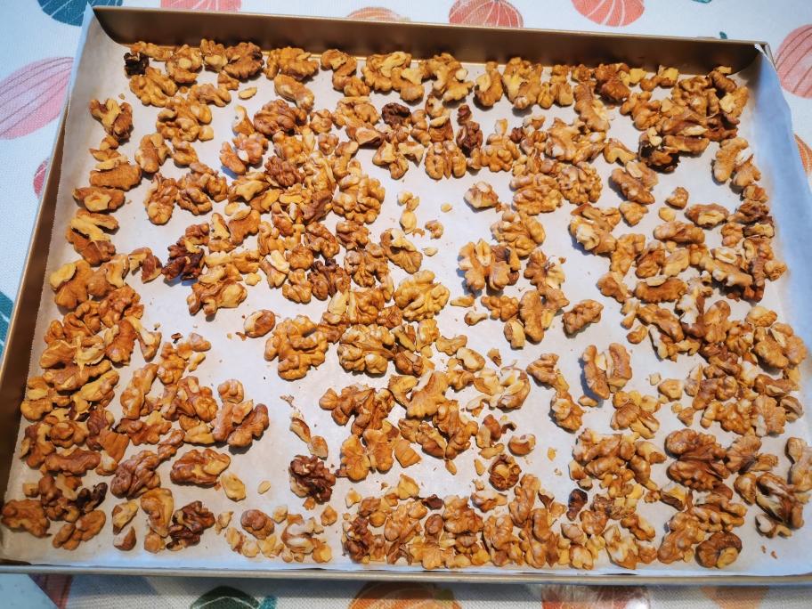 核桃低温轻焙过程特写：带壳核桃平铺于搪瓷烤盘，背景为精准控温烘箱（显示105℃/8min），核桃壳呈自然微裂状，仁色均匀浅金黄，无焦黑斑点