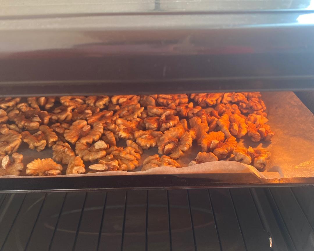 图示:家用烤箱温度计校准显示130℃恒温,新疆纸皮核桃均匀铺于硅胶烤垫上,表面光泽温润无焦痕,计时器显示15分钟,旁边放置食品级密封罐待装盛 家庭厨房中精准烘烤新疆纸皮核桃实景