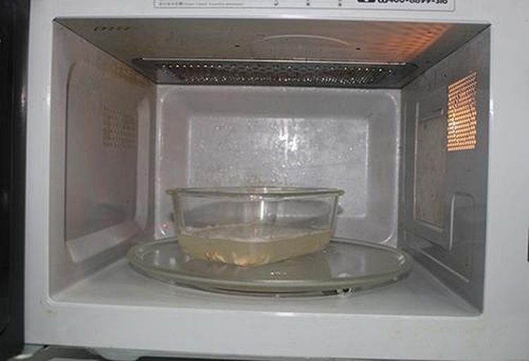 一台家用微波炉内部,中间摆放着一个透明玻璃碗,碗中是一个完整的贝贝南瓜,底部有少量水,南瓜上方覆盖着微波专用保鲜膜,一角留有透气口 微波炉中正在加热的贝贝南瓜,置于加水的玻璃碗内,上方覆盖带透气口的保鲜膜