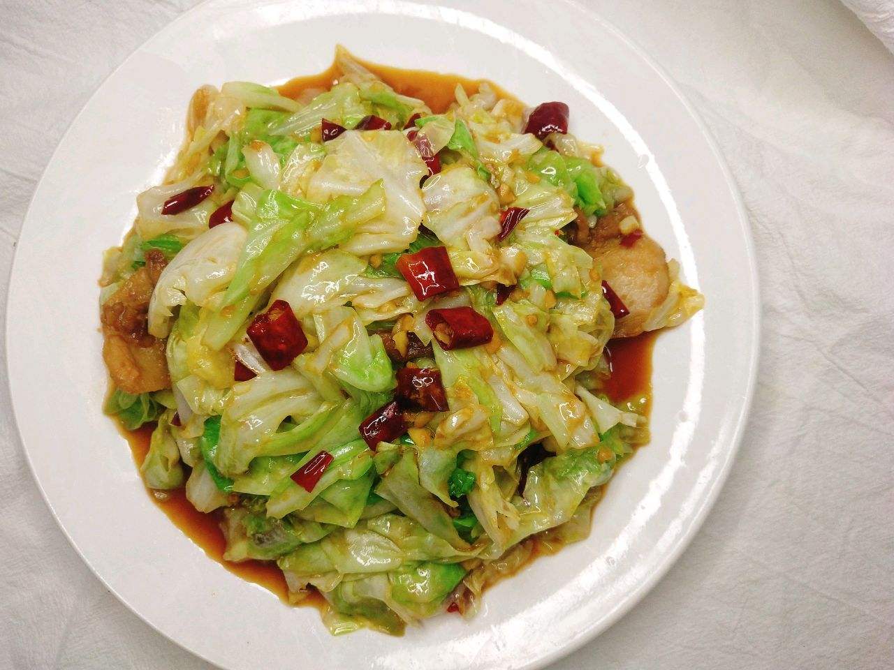 现代中式厨房实景拍摄,展现新鲜包菜从整颗到入锅的烹饪转化过程,强调‘新鲜包菜’在高温快炒中保持形态与色泽的鲜活状态 厨房场景中的新鲜包菜烹饪过程:不锈钢炒锅内油光微泛,青白相间的圆包菜丝正在翻腾,热气升腾,锅铲翻动瞬间可见水汽与菜叶弹跳感,灶台旁摆放整颗未切的新鲜圆包菜作为参照