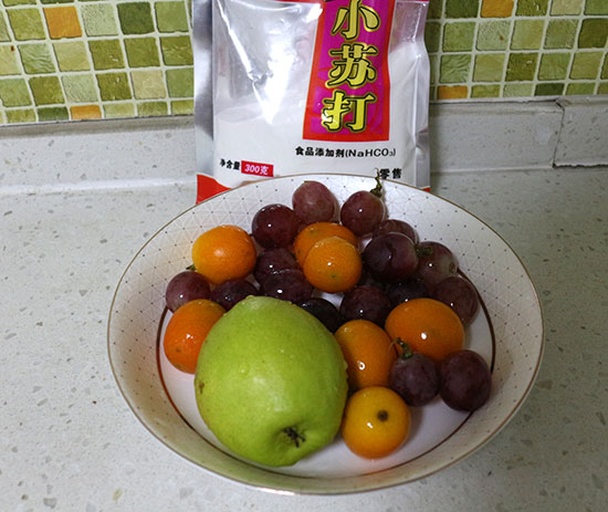 一位家庭主妇在厨房水槽前用清水冲洗金桔,旁边放着小苏打瓶和滤篮,台面上还有几颗洗净的金桔,展现安全食用前的清洗流程 家庭清洗金桔场景图