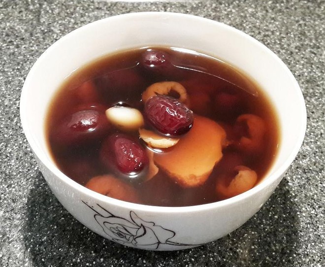 俯拍视角:8颗饱满圆润的黑芝麻汤圆浮于清亮汤水中,表面油润微光,部分汤圆被轻切开,露出深褐色流沙馅心;碗旁配小碟盛放姜丝红糖水与干桂花,整体色调温暖,体现节气食养氛围 煮制完成的黑芝麻汤圆盛于青花瓷碗中特写