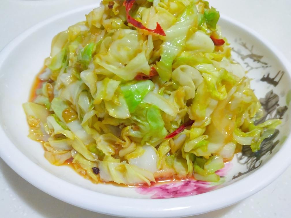 成品装盘特写：青翠包菜片与淡金土豆片交错堆叠，表面油润反光但无浮油，撒少量白芝麻，盘底无汤汁，配不锈钢铲子斜倚盘边