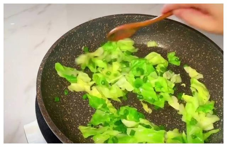 一位家庭主妇在明亮的现代厨房中使用铁锅翻炒松花菜,锅中菜肴呈翠绿色,蒜片金黄,热气腾腾,灶台旁摆放着切好的红椒丝和调料碗,展现真实的家常烹饪过程 家庭厨房中正在翻炒松花菜的场景