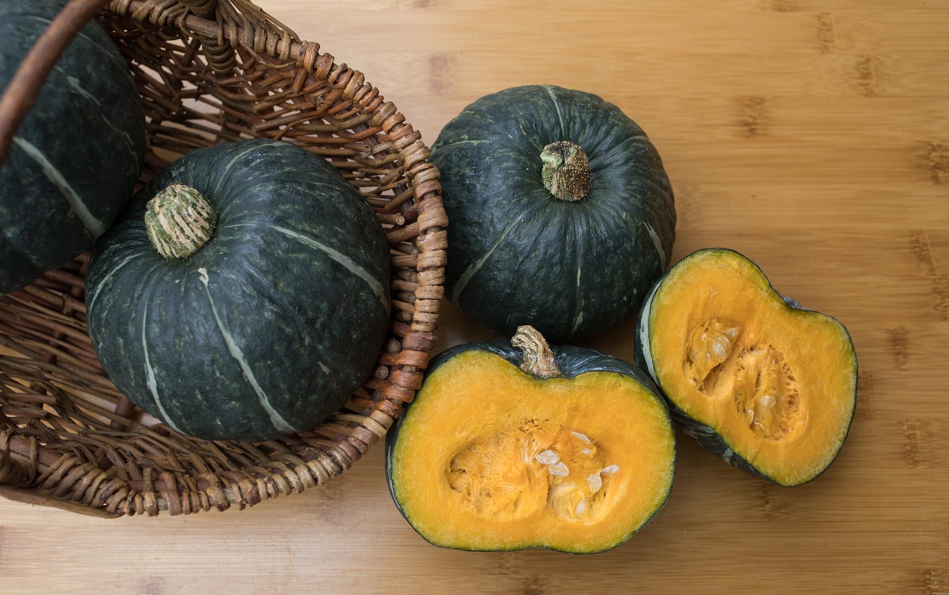 新鲜南瓜堆放在木制农篮中，背景为秋日田野，南瓜表皮呈明亮橙黄色，部分带有绿色藤蔓，光线柔和自然