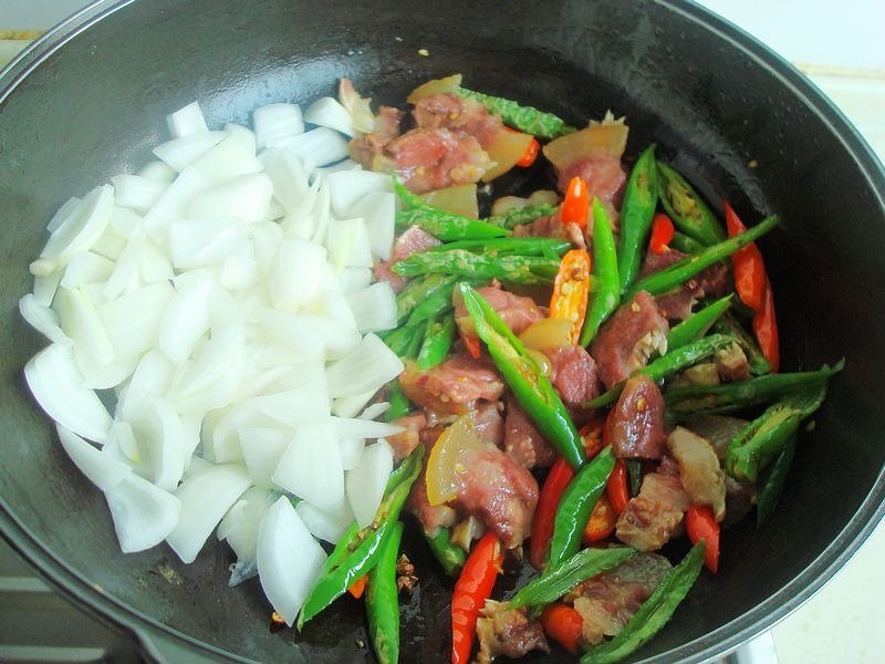 厨房操作台上整齐摆放着去骨鸡腿肉、切好的青尖椒圈、大葱段、姜片和蒜瓣,背景为中式炒锅与调味瓶,展现即将开始烹饪的准备状态 食材摆盘全景图