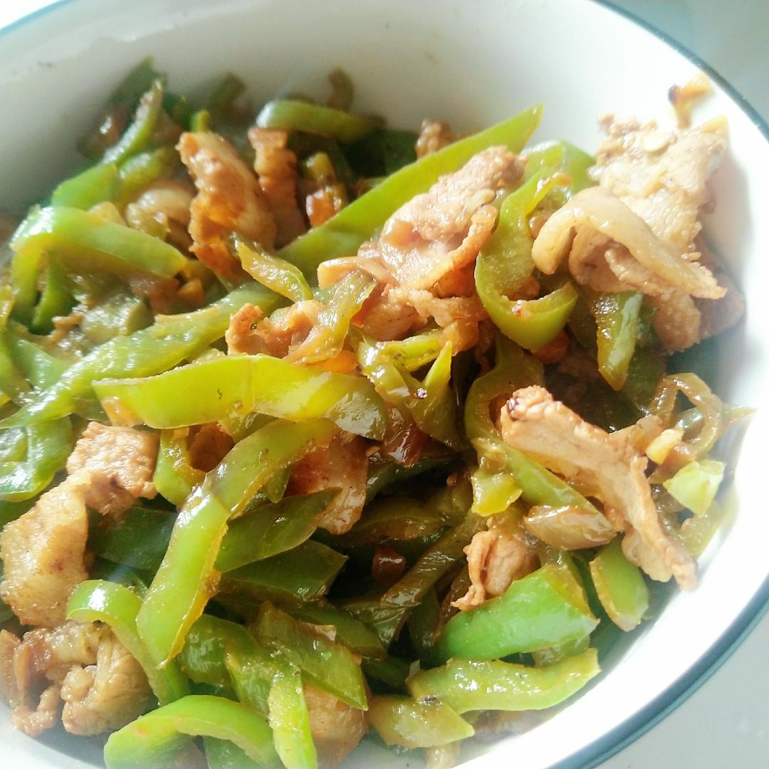 青线椒烹饪场景：中式铁锅中正进行旺火爆炒，青线椒段与薄切猪肉片同炒，椒体微卷泛油光，锅气升腾，配蒜末与姜丝点缀，呈现经典家常风味