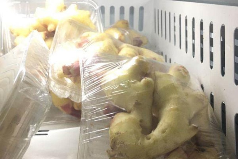 案板上摆放着切好的生姜薄片,旁边有密封袋和冰格模具,生姜正被分装进容器,准备放入冰箱冷冻,场景清晰展示操作步骤 生姜切片冷冻过程