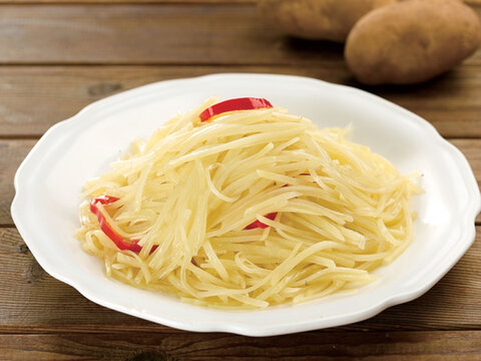 一盘装在白色瓷盘中的尖椒土豆丝，色泽金黄微带焦边，青色尖椒丝清晰可见，背景为木质餐桌，旁边摆放一双筷子和一个小醋碟