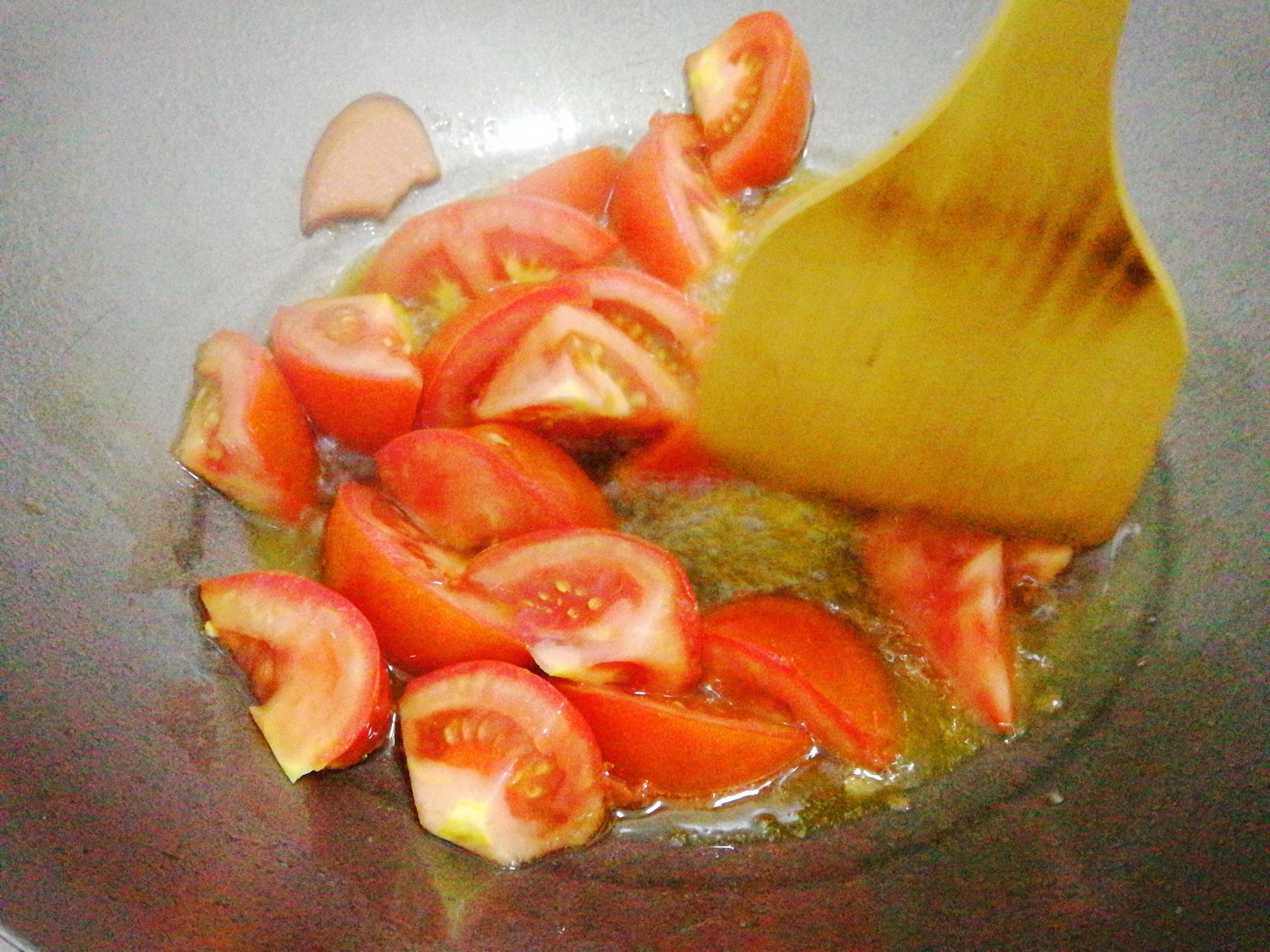 一口铁锅中正在翻炒红色的西红柿块,汁水丰富,部分已融化成浓稠酱状,锅边可见蒜末颗粒,灶台为传统中式厨房,火焰适中 西红柿翻炒过程