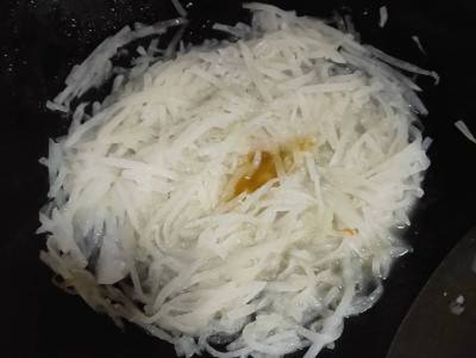 一位厨师在明亮厨房中手持擦丝器将一根已有轻微空心的白萝卜擦成细丝,旁边摆放着碗装全麦粉和鸡蛋,台面上有平底锅和油壶,整体呈现健康料理氛围 厨房场景中正在用擦丝器处理糠心白萝卜用于制作萝卜丝饼