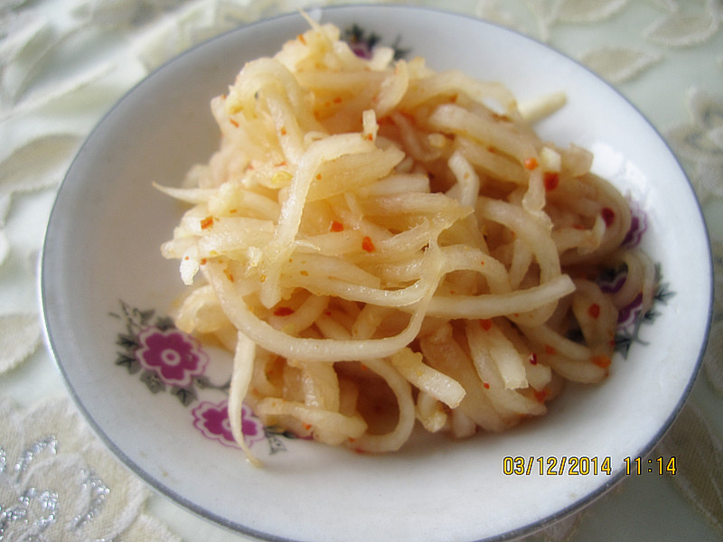 一盘清爽的凉拌青皮萝卜丝,萝卜切成细丝整齐码放,表面撒有碎紫皮蒜末,点缀少量香菜叶,调料汁微透亮,整体呈现清新健康的中式凉菜风格 青皮萝卜丝拌紫皮蒜末的凉菜成品图