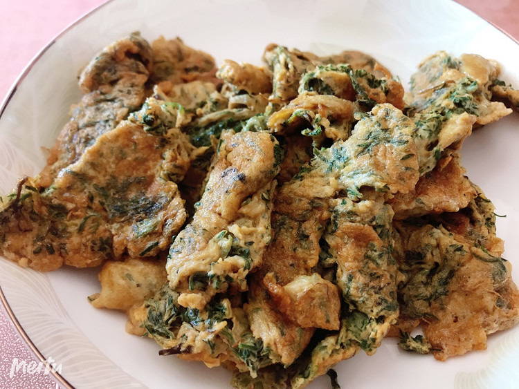 一份金黄色的蒿子杆鸡蛋饼,外皮微焦酥脆,内部可见绿色蒿子杆碎粒均匀分布,摆放在木质砧板上,旁边搭配番茄片和欧芹叶,整体风格自然温馨,适合家庭餐桌场景 蒿子杆炒蛋成品图