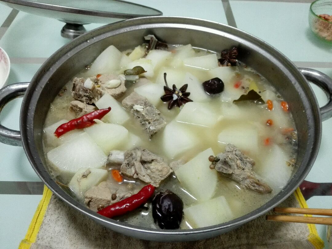 一碗热气腾腾的老黄瓜炖排骨汤,汤色清澈微白,碗中可见切块的老黄瓜(表皮微黄、质地厚实)与猪骨共同炖煮,旁边摆放一根完整的成熟老黄瓜作为对照,整体呈现家庭厨房温馨场景 老黄瓜炖汤实物照片