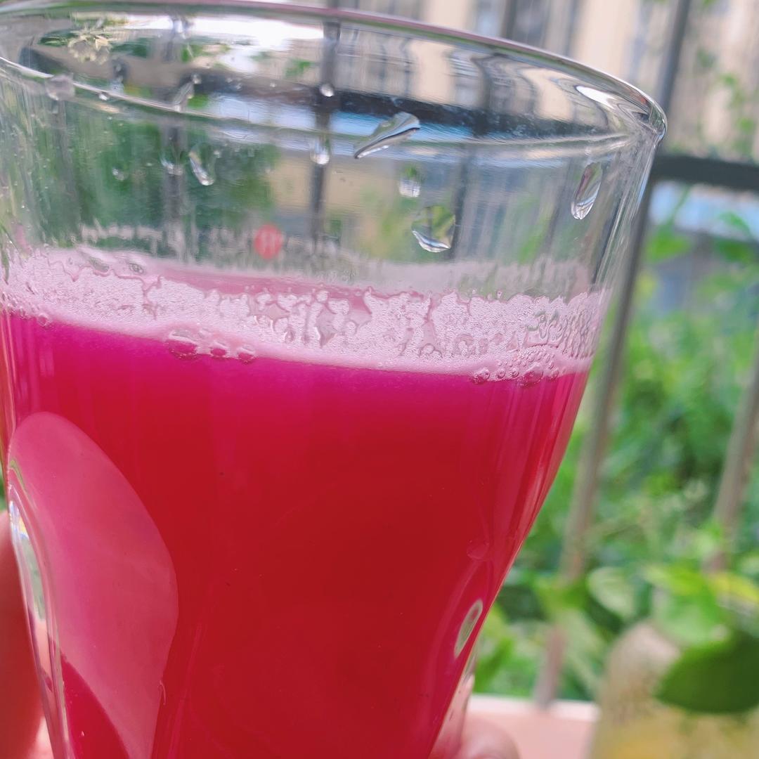 一只透明玻璃杯盛满深紫红色的红提汁,液体清澈透亮,杯壁凝结细密水珠,背景虚化的桌面上摆放着几串新鲜红提果实和半剖开的果粒,展示果汁来源的真实性与天然品质 红提汁特写镜头