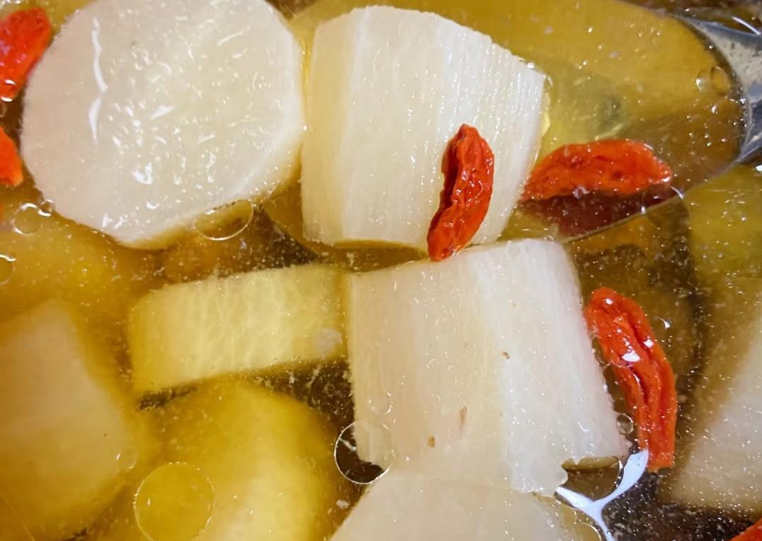 一位中年女性在厨房切白萝卜准备煲汤，操作台上有胡萝卜、枸杞等搭配食材，氛围温馨健康