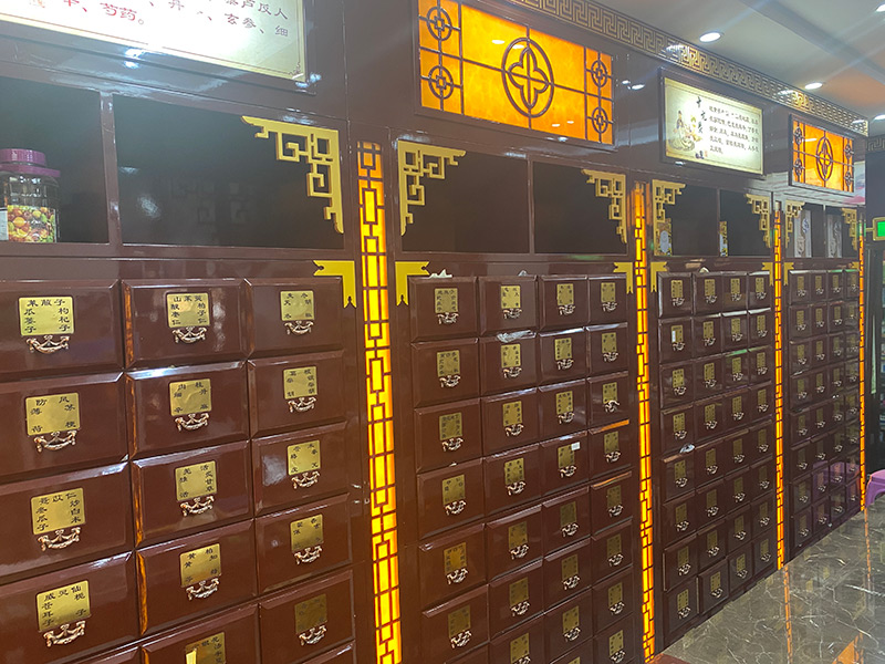 一位身穿传统服饰的中药师正在木质柜台前用铜秤称量黄芪饮片,周围陈列着多个标有药材名称的抽屉柜,空气中仿佛弥漫着淡淡的药香,展现传统中药文化氛围 中药房内药师抓药场景