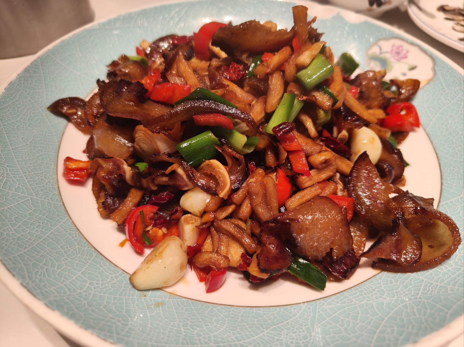 一个中式炒锅正被手持木铲翻动,锅中可见鲜平菇与金针菇交织在一起,表面泛着油亮光泽,周围飘散着蒸汽,灶台为现代嵌入式燃气炉,背景清晰展示调味碗与蒜末等辅料 平菇金针菇在炒锅中翻炒的过程