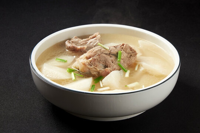 家庭食养白萝卜羊肉汤摆盘摄影:青花瓷深碗盛装,汤体透亮无油膜,羊肉呈浅褐色酥软状,白萝卜块呈半透明玉质,边缘微带琥珀色汤汁浸润;表面点缀6颗饱满红枸杞与3根嫩绿香菜叶;背景为原木餐桌与米白色亚麻餐巾,体现中式健康饮食场景 家庭厨房场景中的白萝卜羊肉汤盛装图,青花瓷碗内汤品清澈,羊肉酥软、萝卜晶莹,撒少许枸杞与香菜,背景为木质餐桌与棉麻餐巾