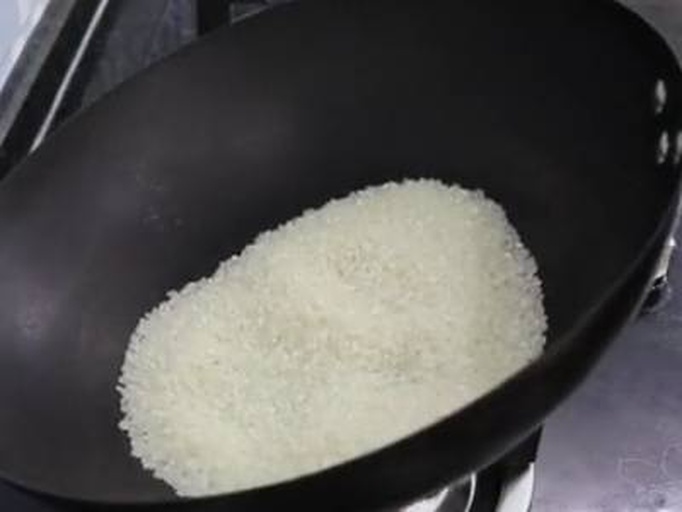 电饭煲内胆中可见黑色的黑豆与白色大米均匀混合,表面有轻微气泡翻滚,蒸汽从边缘缓缓升起,锅盖半开状态,显示烹饪正在进行中,背景为厨房台面 电饭煲中正在烹饪的黑豆饭特写