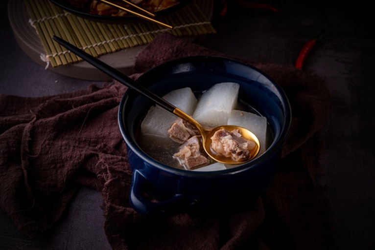 一锅正在炖煮的白萝卜排骨汤,汤色乳白,白萝卜块清晰可见,旁边配有切好的葱姜和香料,背景为中式厨房灶台 白萝卜烹饪场景
