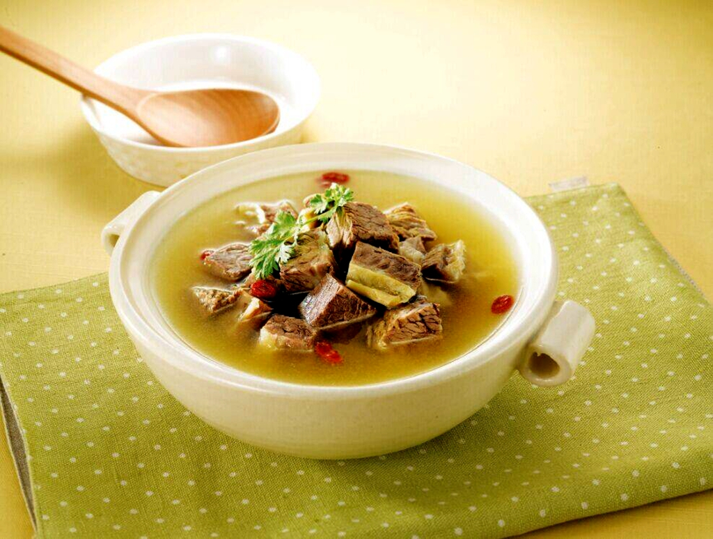 暖光俯拍:深褐色浓郁汤汁中,琥珀色牛肉块纹理清晰,金黄土豆块完整绵软,乳白色山药块粉糯微透,点缀翠绿葱花与几粒枸杞,汤面浮着细密油星,散发温润光泽,碗边搭一小碟蘸料(蒜泥+香醋+辣椒油) 山药土豆牛肉炖成品特写