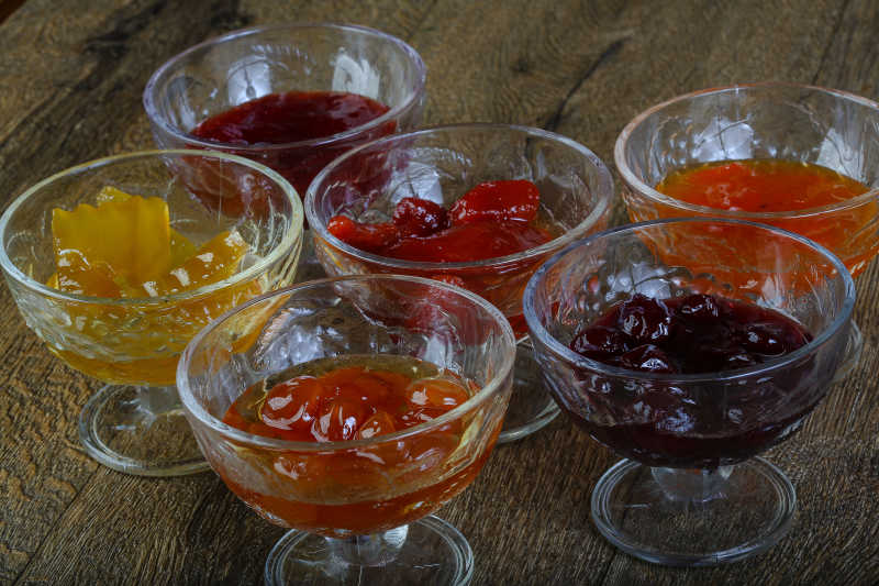 一张木质餐桌上摆放三个透明玻璃碗,分别盛放红色辣油酱、浅黄色酸奶芝麻酱和橙黄色泰式柠檬汁,旁边是一盘切成斜片的清脆小黄瓜,整体呈现清新诱人的美食氛围 多种小黄瓜酱料成品展示