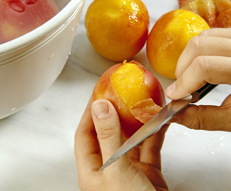 一个新鲜桃子被放入冒着热气的水中,旁边有划好十字口的桃子特写,背景为厨房台面,展示热水烫桃去皮的第一步操作场景 桃子热水烫后去皮过程