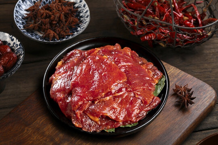 一位家庭厨师正在厨房操作台前将自制五香粉撒入炖煮中的红烧肉锅中,蒸汽袅袅升起,旁边放置玻璃罐装的各种香料原料,展现从原材到应用的全过程,强调天然、健康、可追溯的理念 家庭厨房中使用五香粉烹饪场景
