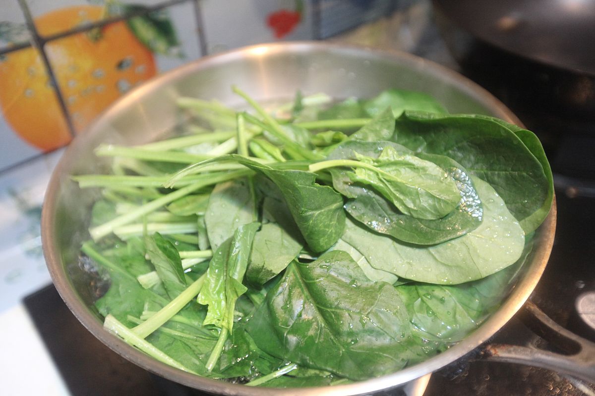 正在煮制的大叶菠菜汤,锅中汤汁沸腾,蛋花与菠菜交融 锅中正在煮沸的大叶菠菜汤,锅边可见绿色汤汁与蛋花交融