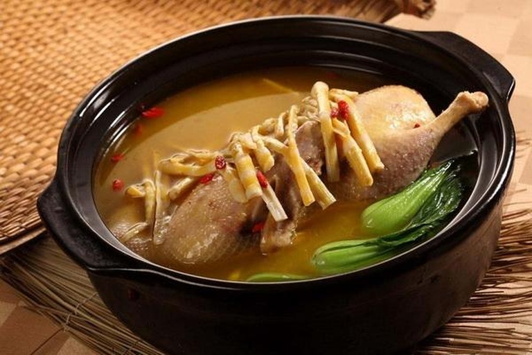 一口深褐色陶制砂锅正置于炉灶上,锅盖微启,冒出袅袅热气;锅内可见金黄色的老鸭块与洁白的雷笋片交错翻滚,汤色呈淡乳白色,清澈透亮,周围摆放着姜片和枸杞 砂锅中炖煮中的雷笋老鸭汤