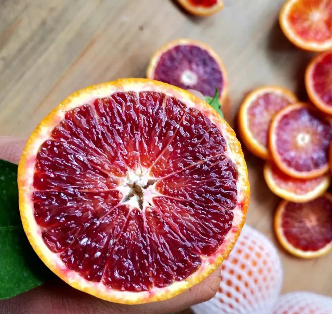 一颗成熟的四川资阳血橙被横向切开,露出鲜艳的紫红色果肉,呈放射状条纹分布,汁水充盈,果粒饱满透明,背景为木质砧板,突出其天然高品质特征 血橙切面特写展示红色果肉