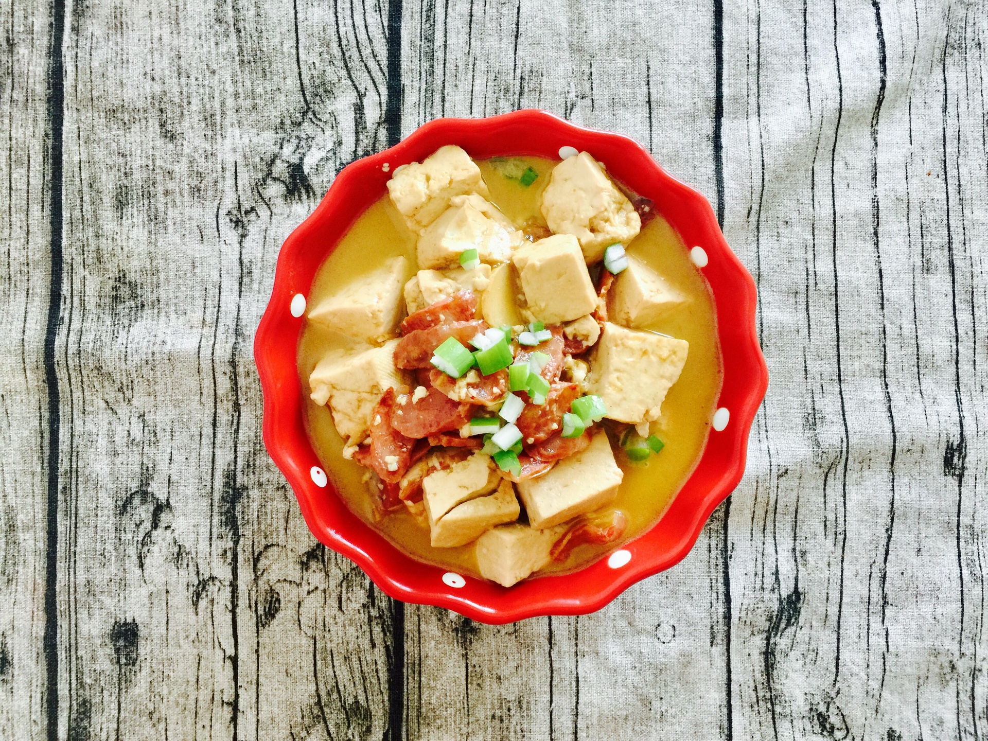 一盘红椒丁与金黄色豆腐块混合的菜肴,置于浅口圆盘中,红椒鲜艳,豆腐表面微焦,点缀绿色葱花,旁边配有米饭和筷子,展现家常用餐场景 红椒炒豆腐装盘图