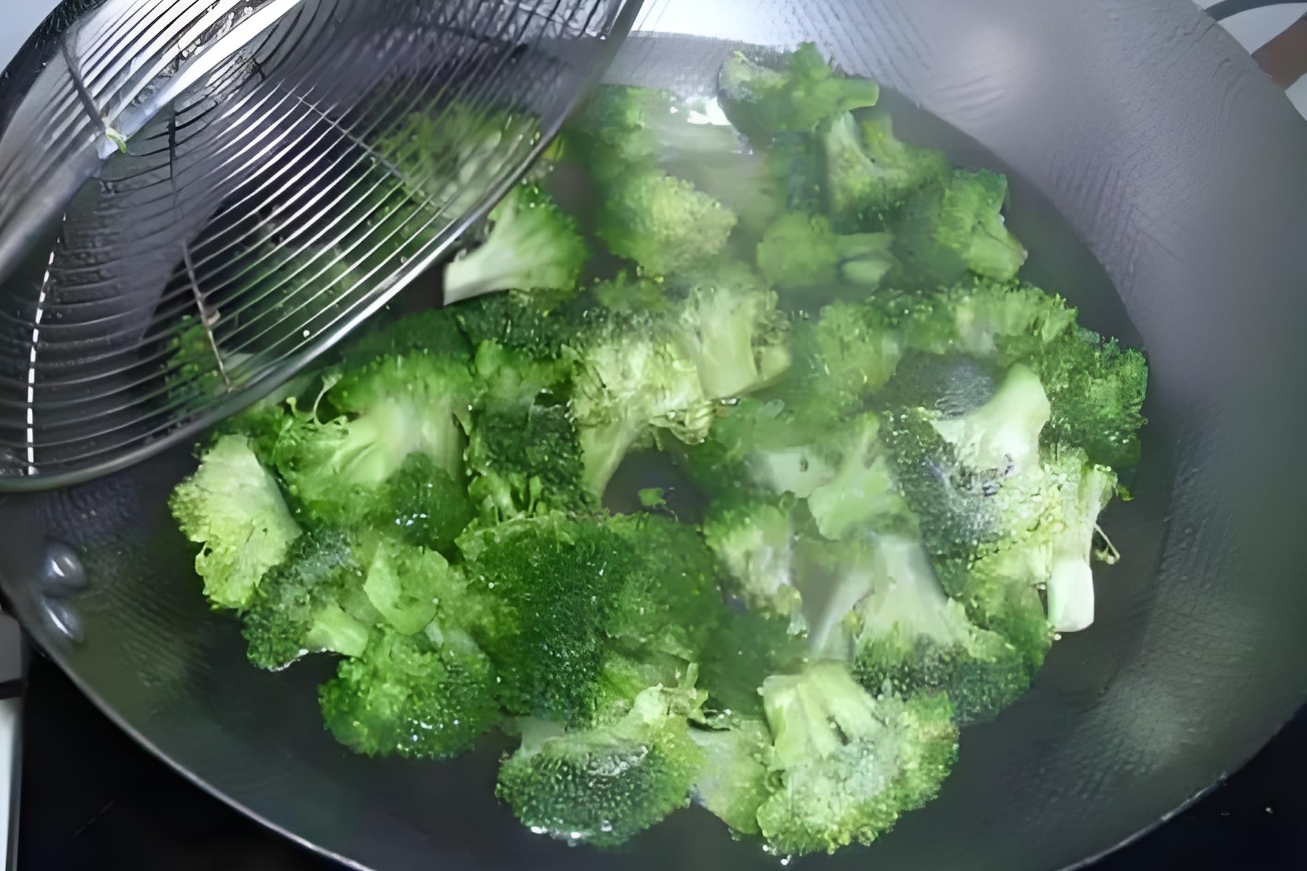 西兰花在沸水中焯烫的过程，花朵呈鲜绿色，水面有轻微气泡，旁边放置一碗冰水用于冷却