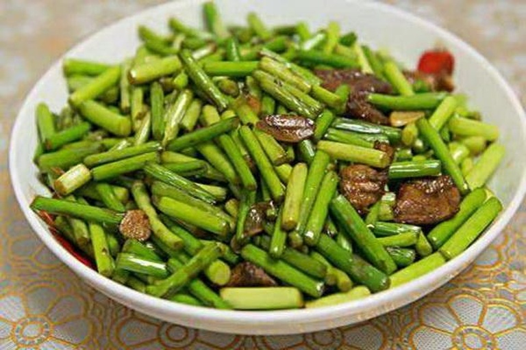 一盘刚出锅的蒜薹炒土豆盛放在白色瓷盘中,土豆条呈金黄色微焦边缘,蒜薹碧绿鲜亮,整体油润有光泽,表面覆盖一层薄薄的透明芡汁,旁边点缀少许红椒丝作为色彩对比 蒜薹炒土豆成品特写