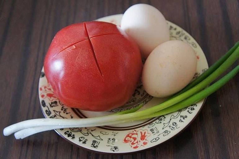 厨房操作台上整齐摆放着紫红色外皮的新鲜洋葱、三个土鸡蛋、小碗中的调料(盐、糖、生抽)、一把葱花以及一双筷子和炒锅,背景为明亮整洁的厨房环境 食材摆盘图