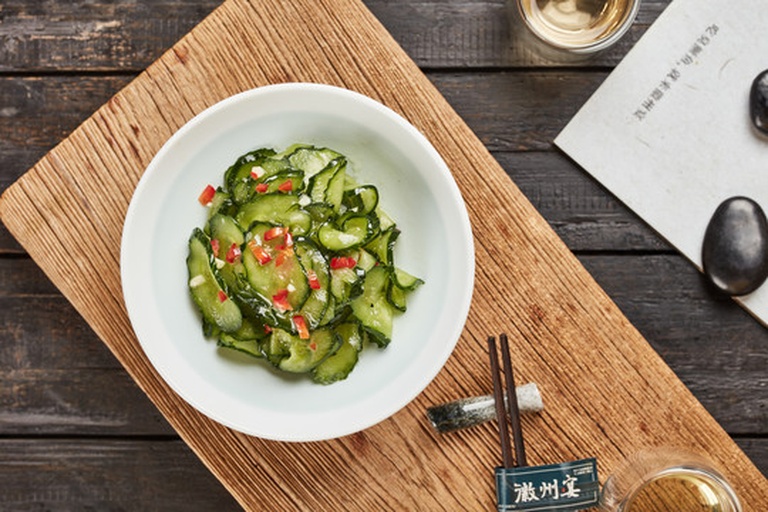 一张木质餐桌上展示三种不同风格的黄瓜西红柿料理：传统凉拌、西式酸奶沙拉、中式热炝版本，配有餐具和柠檬片装饰