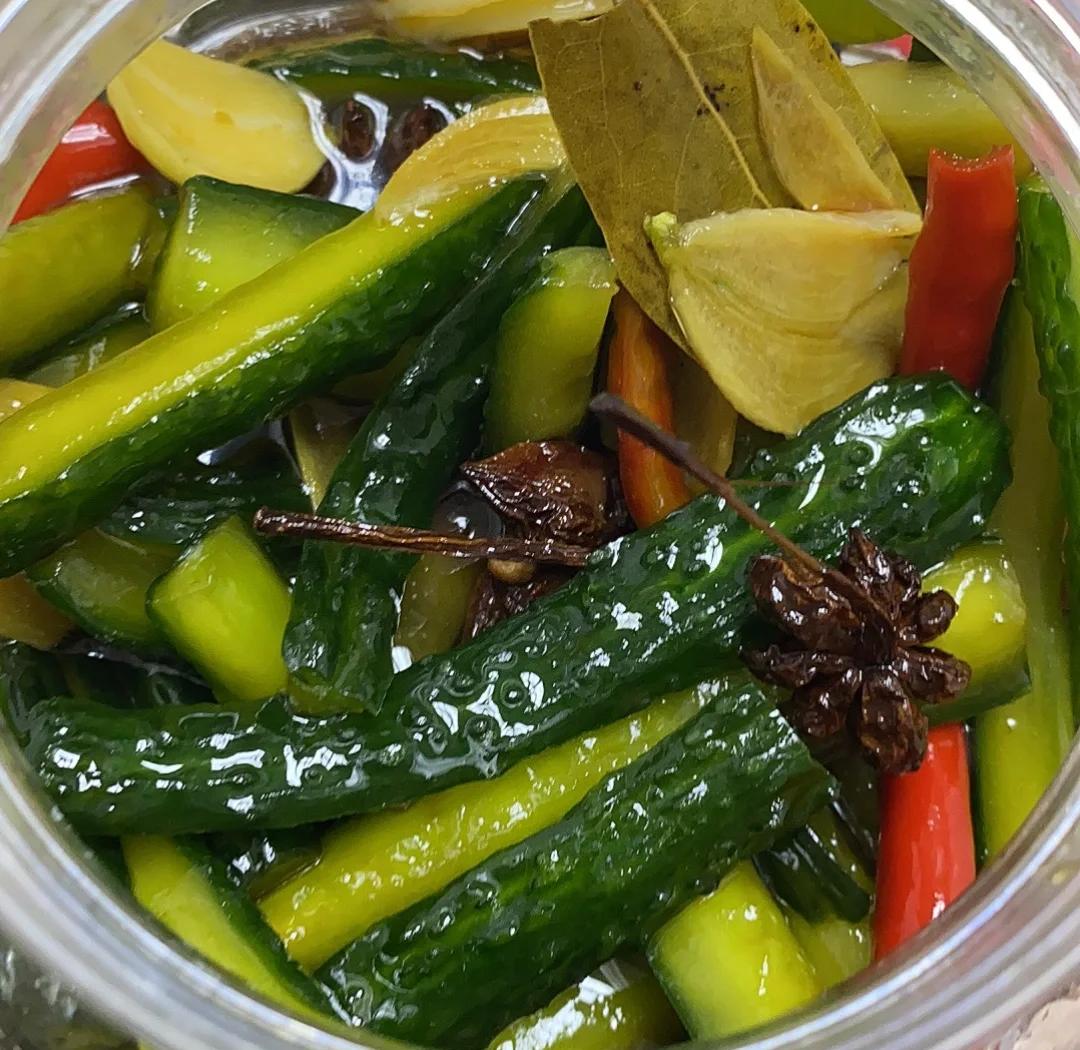 俄罗斯传统乡村腌制作坊内景,木质大桶中浸泡着大量新鲜莫尼卡F1小黄瓜,工人正在添加大蒜、莳萝、橡树叶等天然香料,背景可见堆叠的玻璃罐装成品,体现传统工艺与自然风味的结合 俄罗斯乡村腌制工坊场景