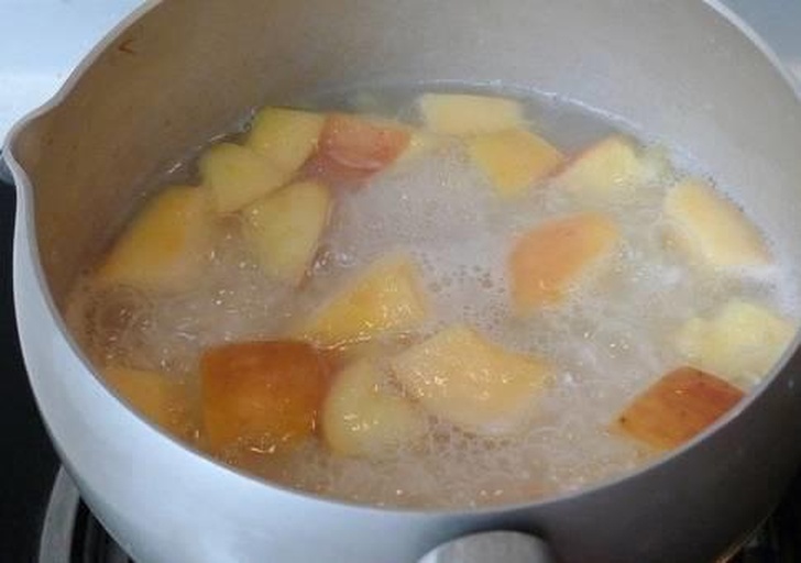 一个不锈钢锅中盛有清水,几片去皮的苹果切片正在水中加热煮制,水面微微冒泡,背景为厨房灶台,光线柔和自然 苹果切片放入锅中加水煮制的过程
