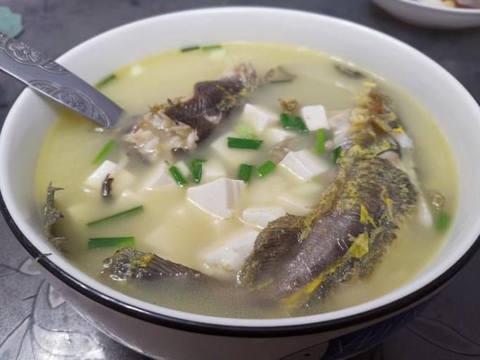 一碗热腾腾的白萝卜鲫鱼汤,汤色呈乳白色,碗中有鲫鱼块与白萝卜丝,旁边配有筷子和小碟,背景为浅色餐桌,体现家庭温馨氛围 白萝卜鲫鱼汤成品图
