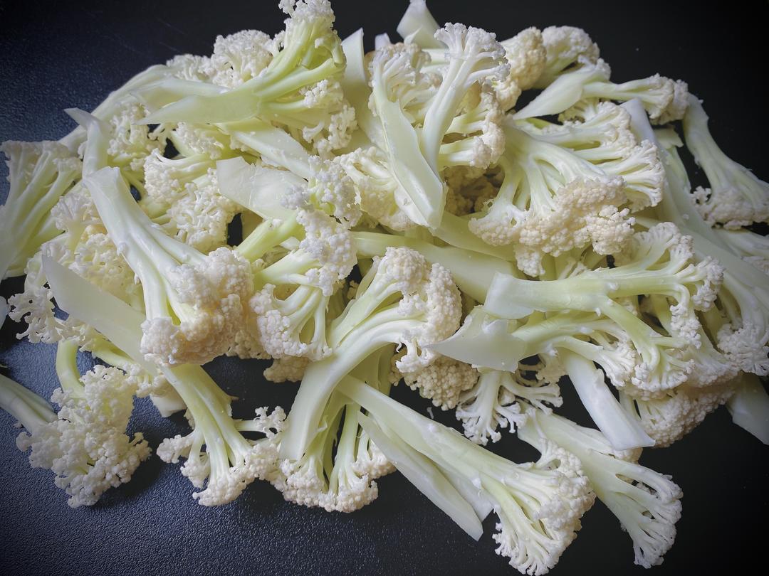 新鲜菜花被放置在案板上,用刀从根部纵向切开,露出密集洁白的花蕾。旁边有清水盆和小刷子,显示正在清洗缝隙中的泥沙 菜花清洗与切分过程