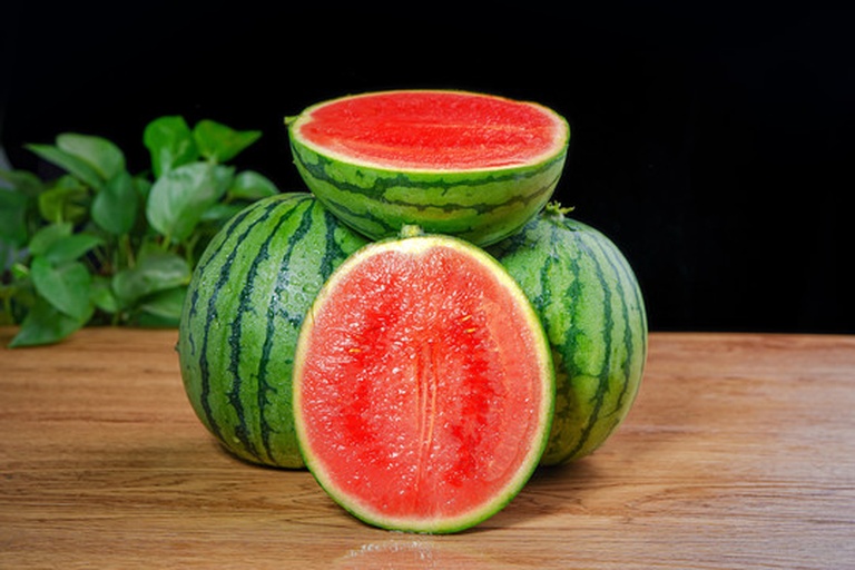 一个完整的西瓜红蜜薯被横向切开,露出内部鲜艳的橙红色薯肉,切面光滑细腻,周围摆放着几片切好的薯块,背景为田园风格木质桌面,光线柔和自然 西瓜红蜜薯切面特写