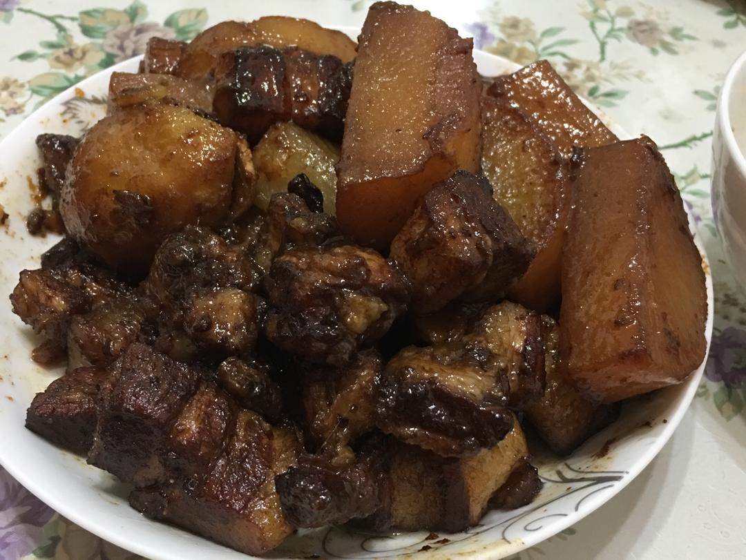 深色陶瓷炖锅中盛满红亮油润的烧肉菜肴,肥瘦相间的五花肉块与半透明的青萝卜块交错分布,表面泛着光泽,几根葱花点缀其间,蒸汽袅袅升起,展现热腾腾的家常美味氛围 青萝卜烧肉成品特写